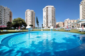 Ein Swimmingpool mit Liegestühlen, umgeben von Hochhäusern und einem klaren Himmel.