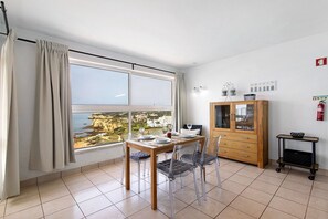 Ein Essbereich mit Tisch für vier Personen, einem Holzschrank und Blick auf das Meer.
