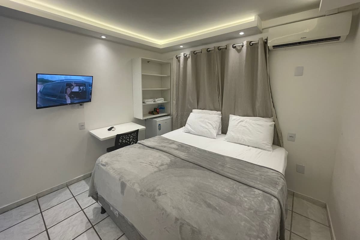 A modern bedroom with a large bed, a TV mounted on the wall, a small desk, and a built-in wardrobe.