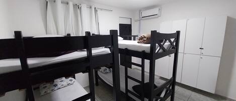 Un dormitorio con literas, un escritorio, una silla, un armario y un equipo de aire acondicionado.