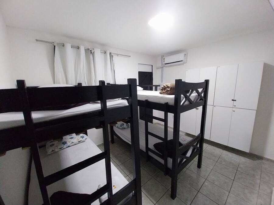 A dormitory room with bunk beds, a desk, a chair, a wardrobe, and an air conditioning unit.