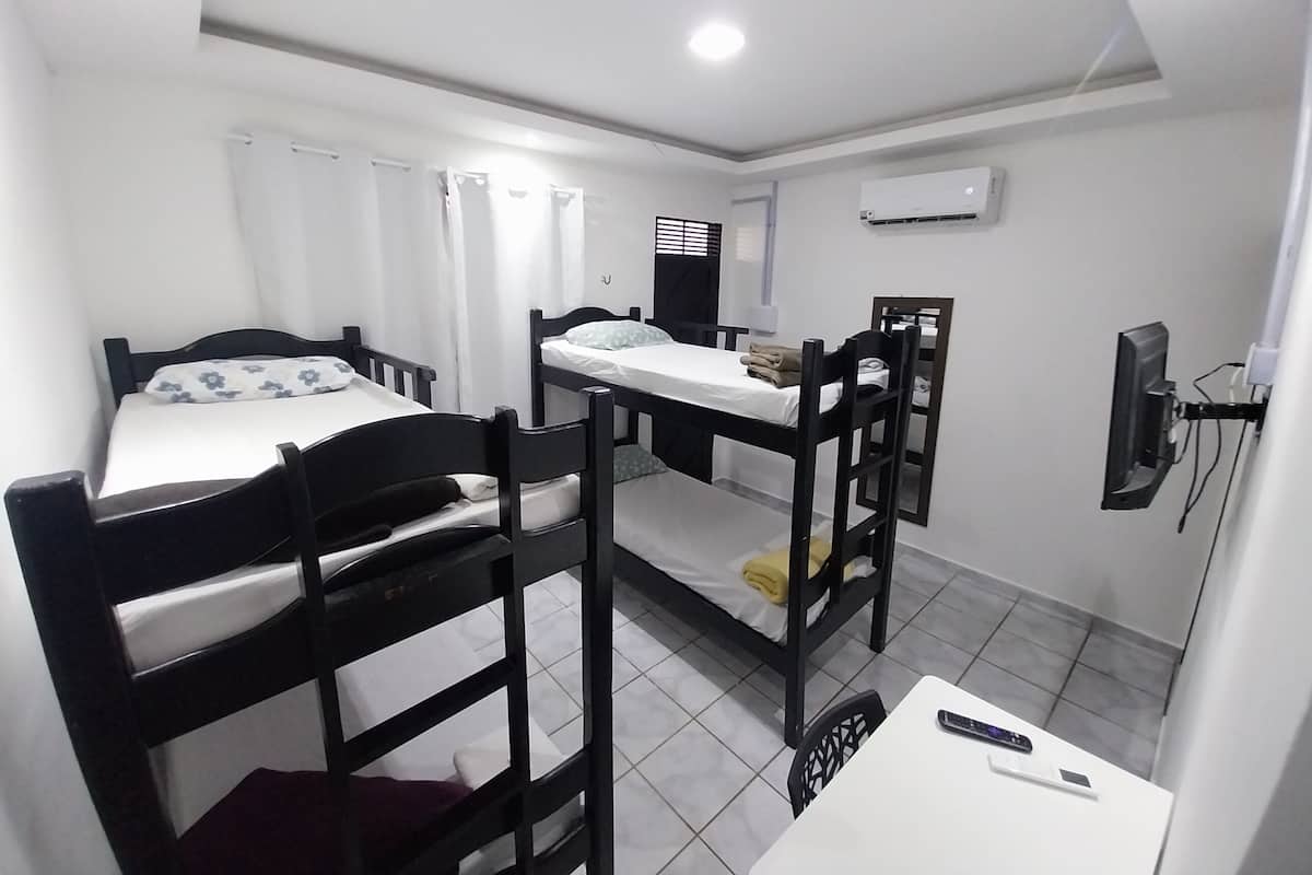 A compact room with two bunk beds, a small table, a TV mounted on the wall, and a window with curtains.