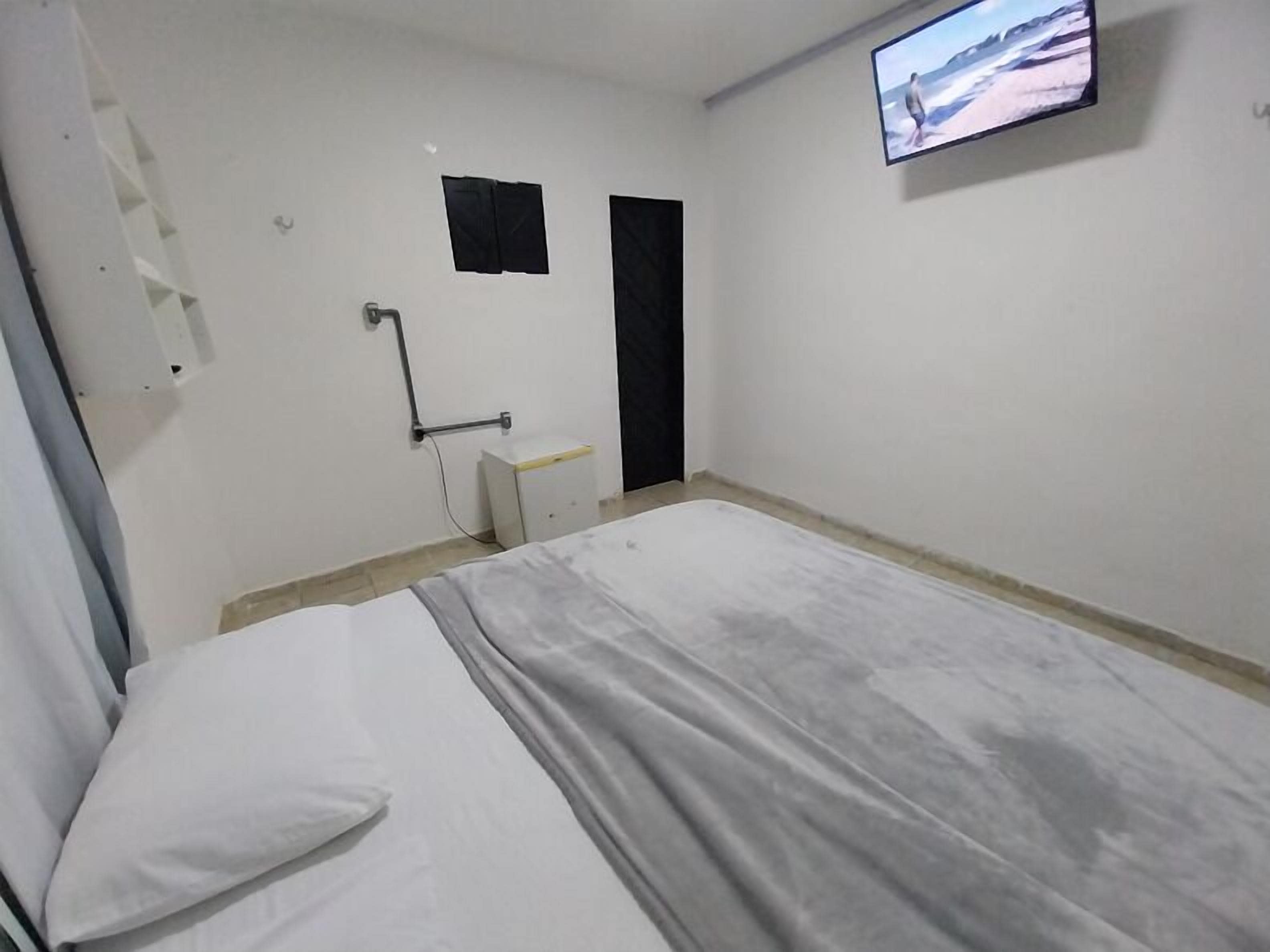 A simple, unadorned room with a bed, a television mounted on the wall, and a door.