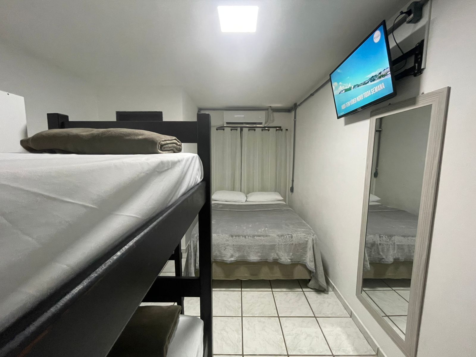 Een kleine, compacte kamer met twee stapelbedden, een aan de muur bevestigde televisie en een spiegel aan de rechterkant.