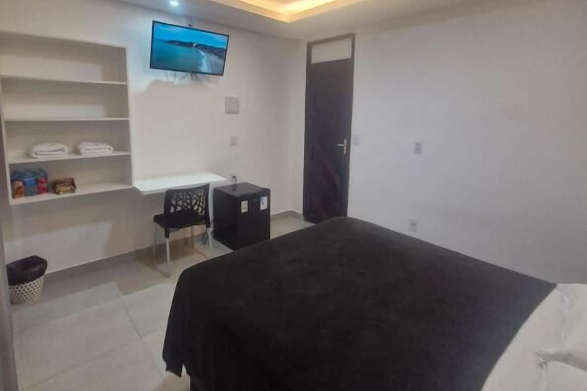 A modern hotel room with a large bed, a desk with a chair, a TV mounted on the wall, and a door.
