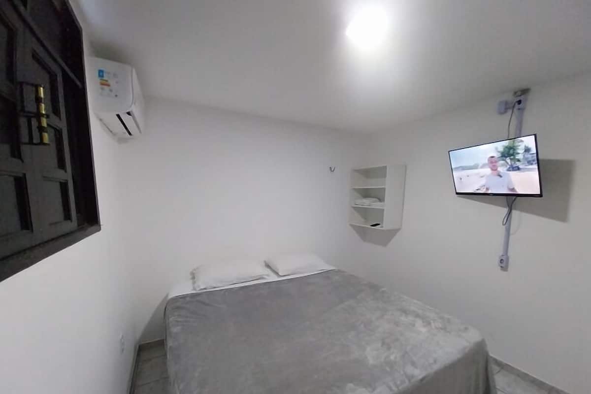 A bedroom with a bed, a TV mounted on the wall, and a window with a view.