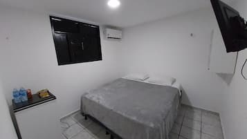 Una habitación pequeña y limpia con una cama, un escritorio, una ventana y un equipo de aire acondicionado.