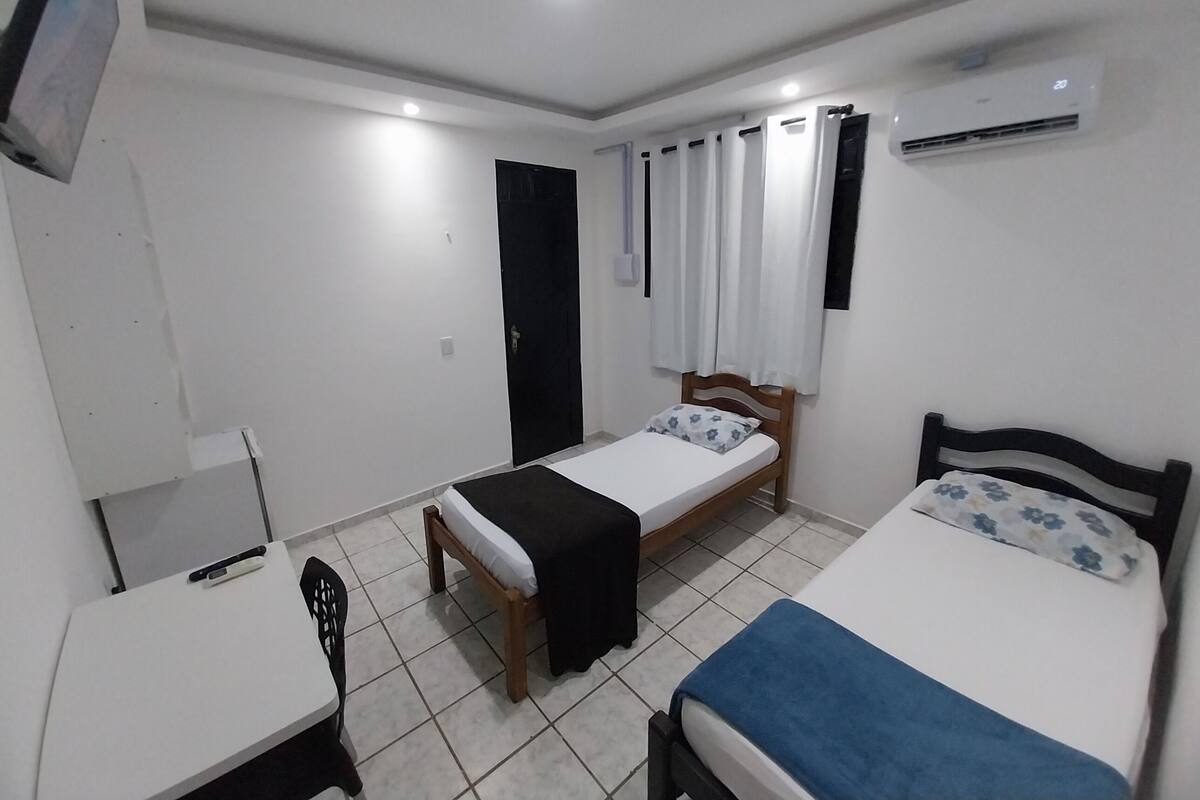 A small, clean room with two single beds, a desk, and a chair.