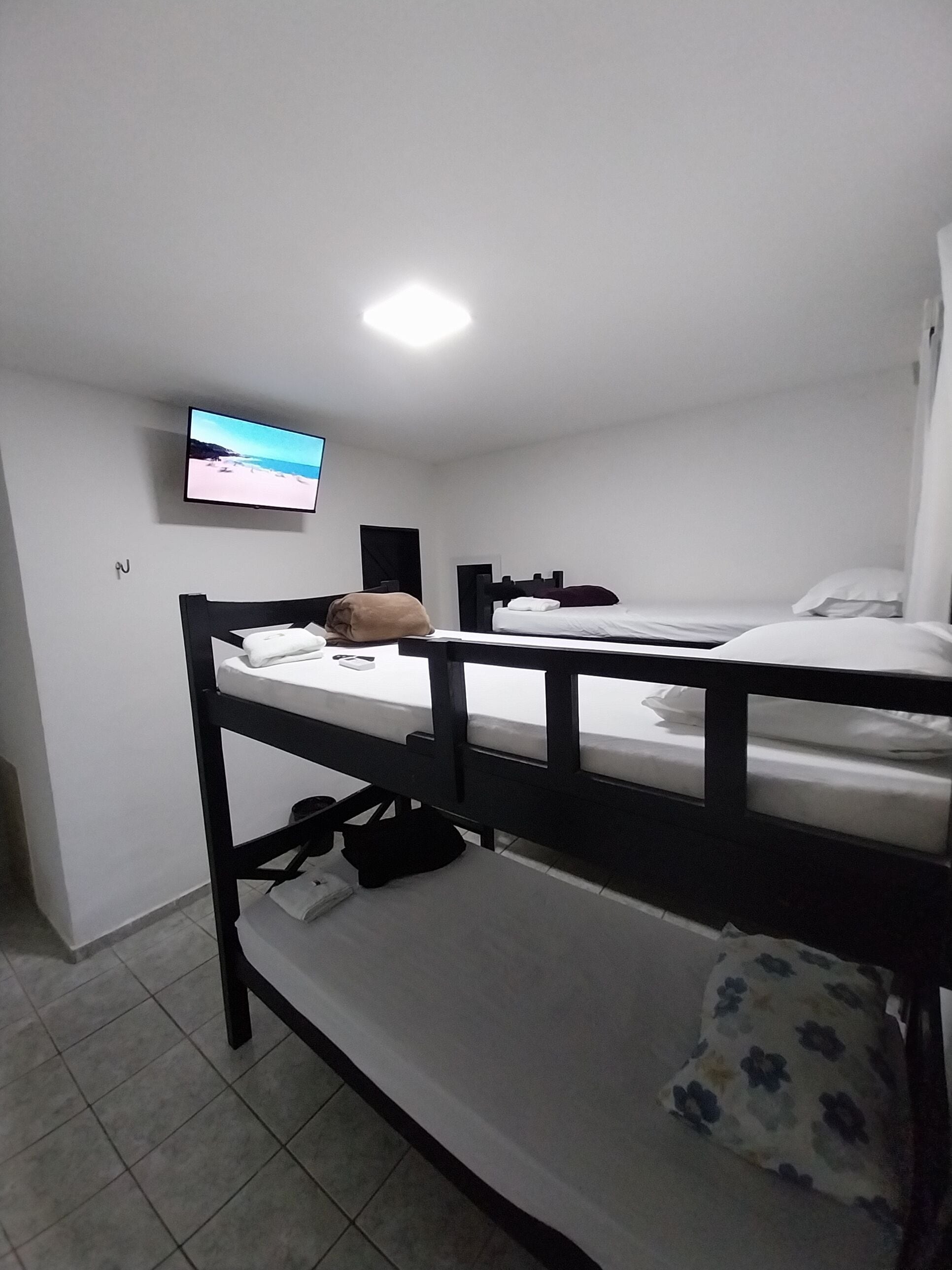 Habitación tipo dormitorio con literas, un televisor de pantalla plana montado en la pared y suelo de baldosas.