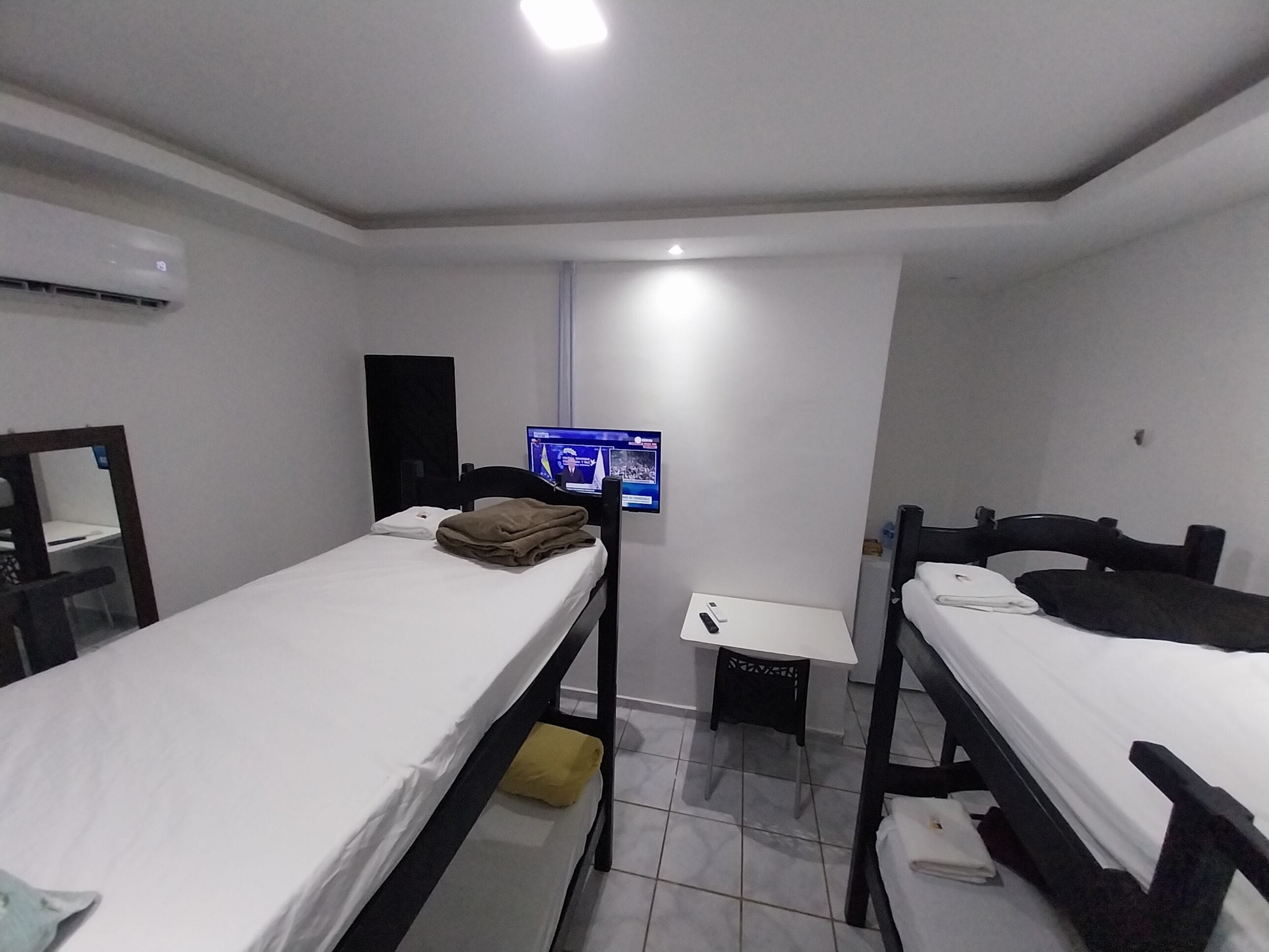 Ein kleines, sauberes Zimmer mit zwei Einzelbetten, einem Schreibtisch, einem Stuhl und einem Fernseher an der Wand.