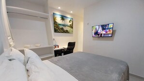A hotel room with a bed, a desk, a chair, a TV, and a painting on the wall. - Pousada Dunas Natal (Natal)