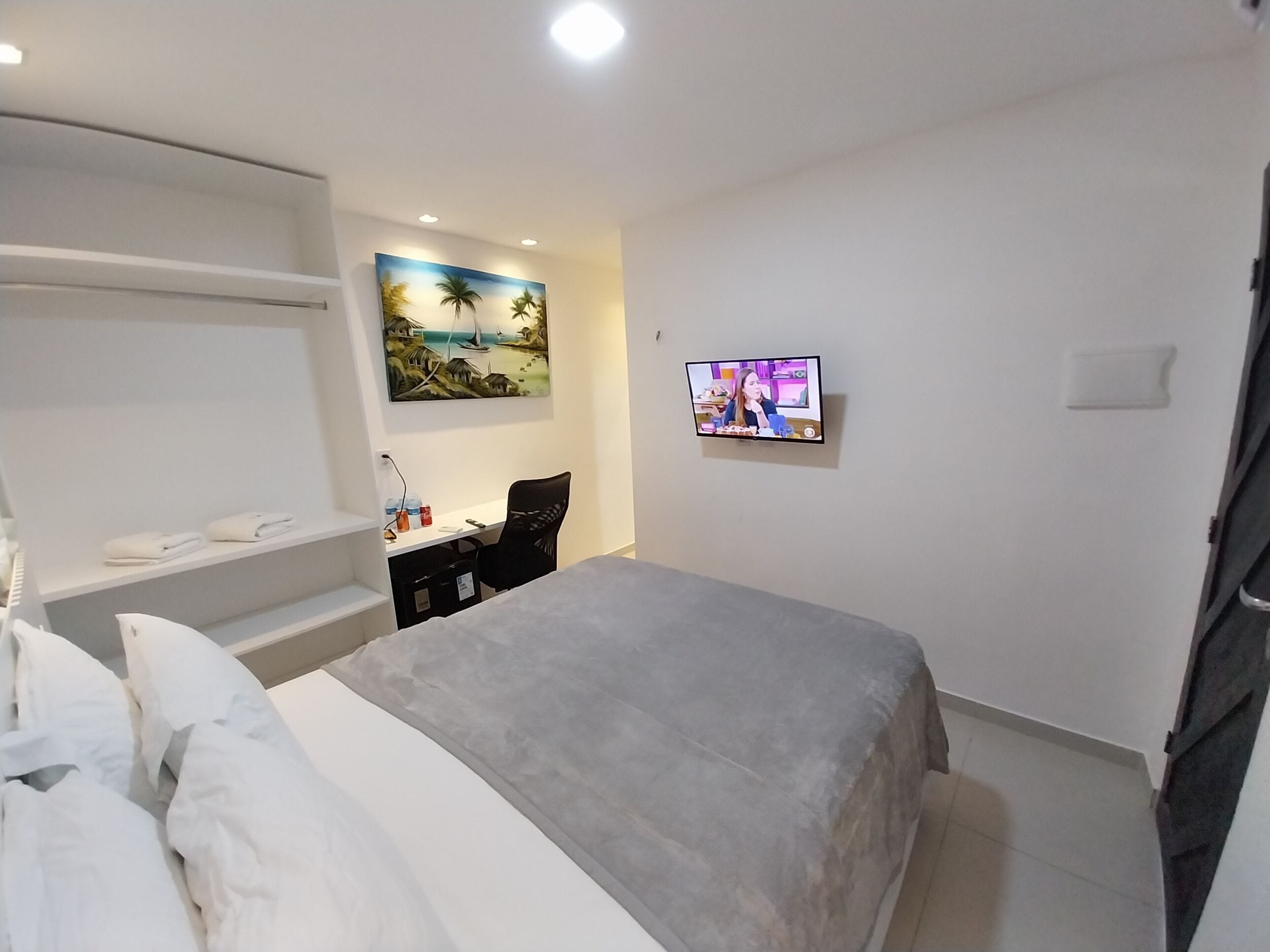 Un dormitorio con cama, escritorio, silla, televisor y un cuadro en la pared.