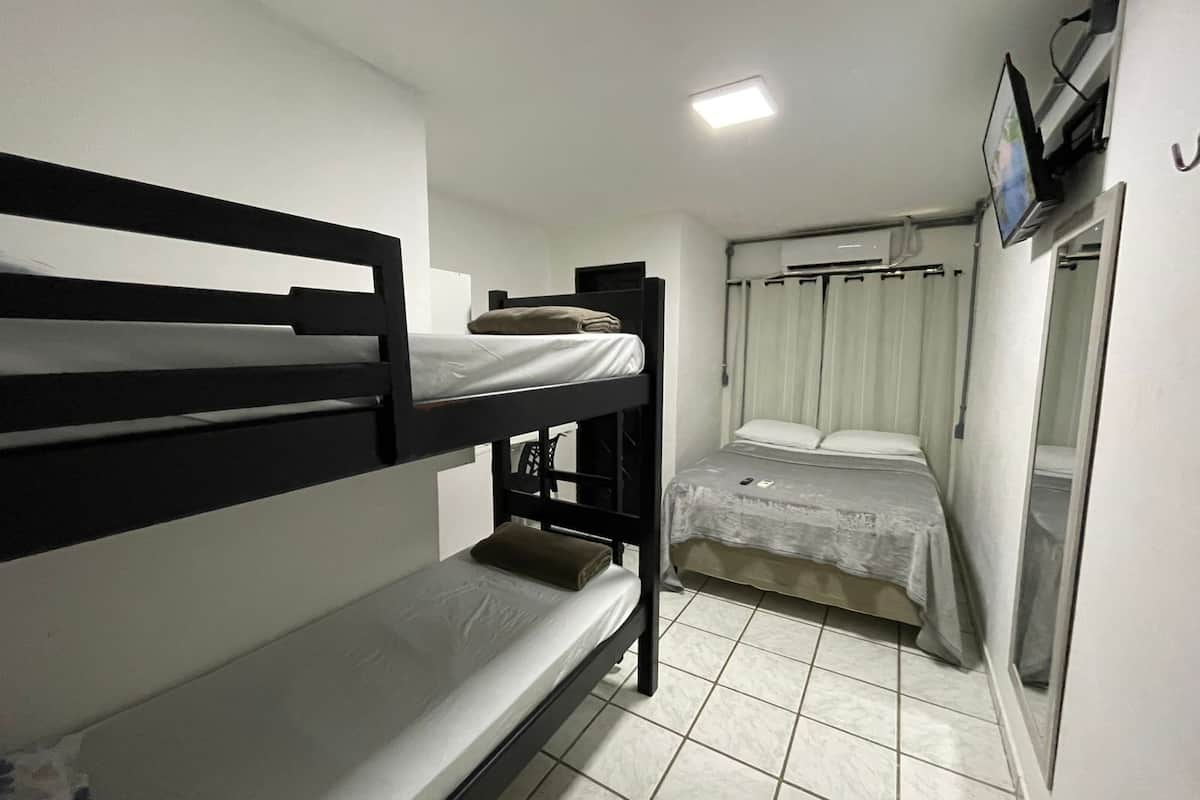 A bunk bed room with a small desk, a bed with a white mattress, and a window with curtains.