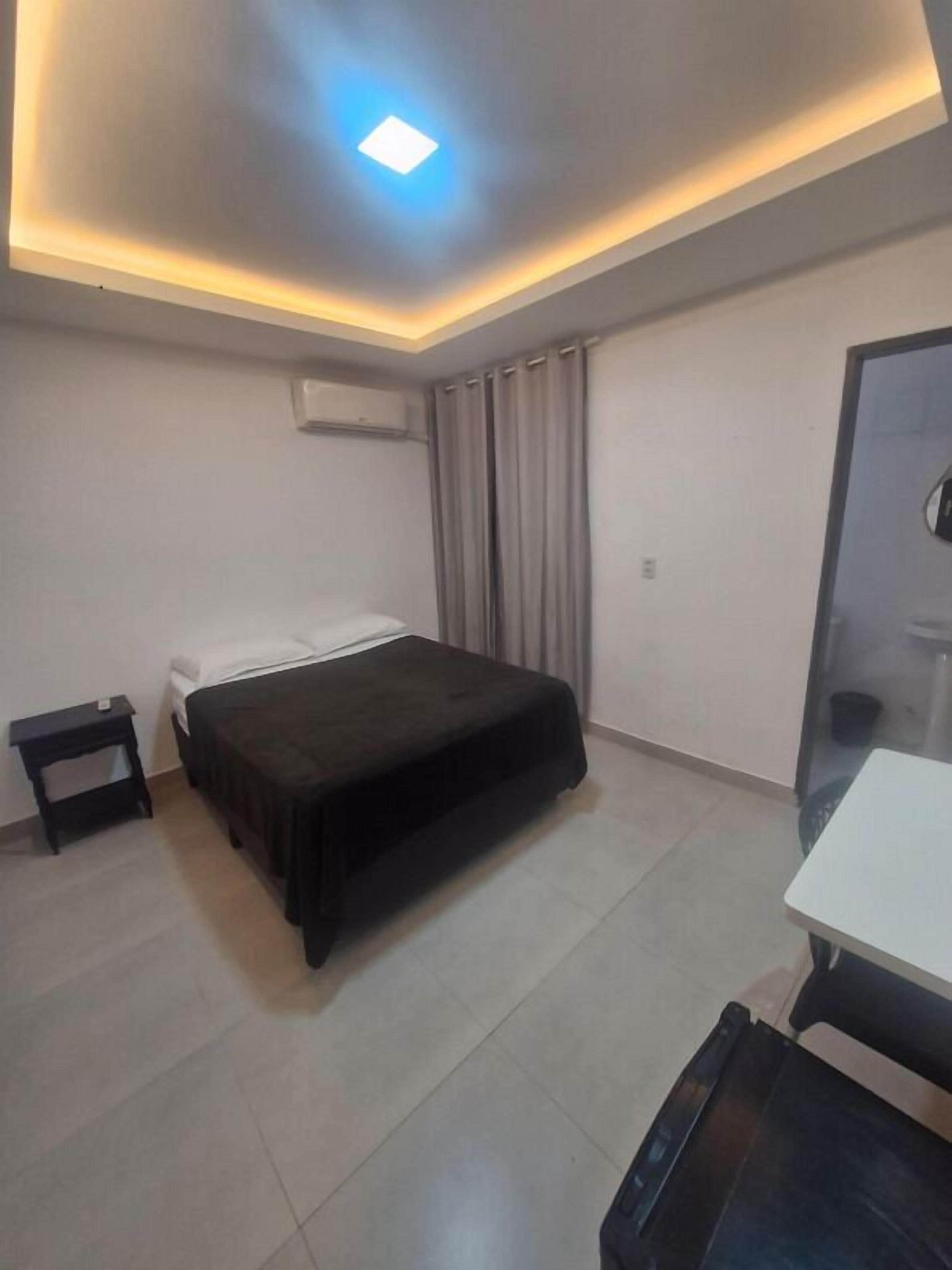 A hotel room with a bed, a small bedside table, a desk, and a chair.