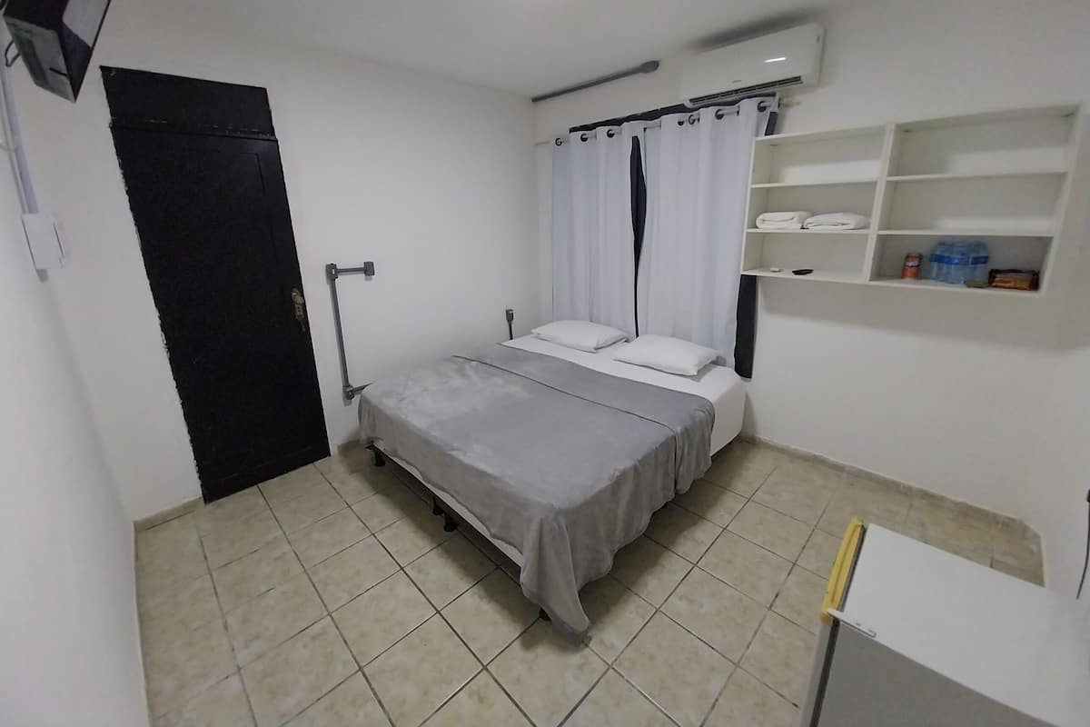 A small, clean room with a bed, a shelf with toiletries, and a door.