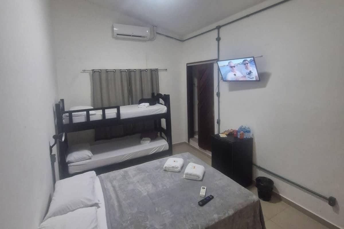A dormitory-style room with bunk beds, a flat-screen TV mounted on the wall, and a ceiling fan.