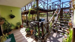 A wooden deck with a metal staircase, surrounded by potted plants and a car in the background. - Pousada Dunas Natal (Natal)