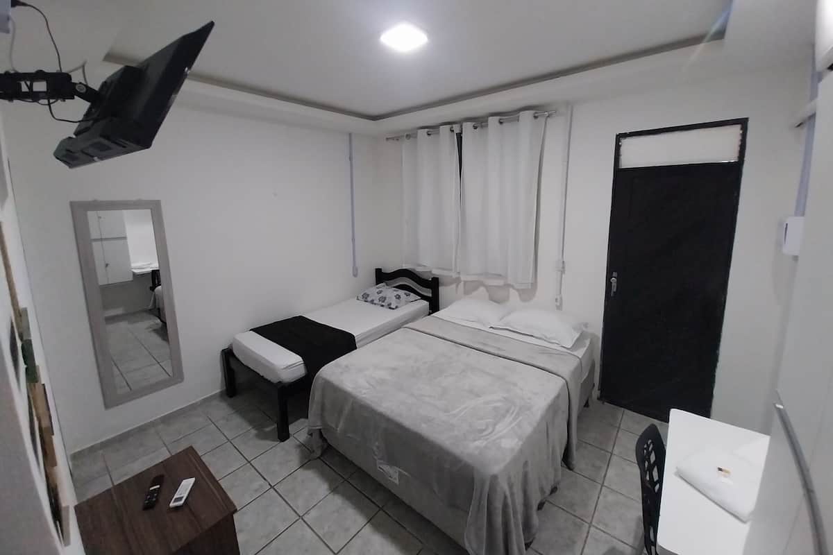 A small, clean room with two single beds, a desk, a chair, a mirror, and a door.