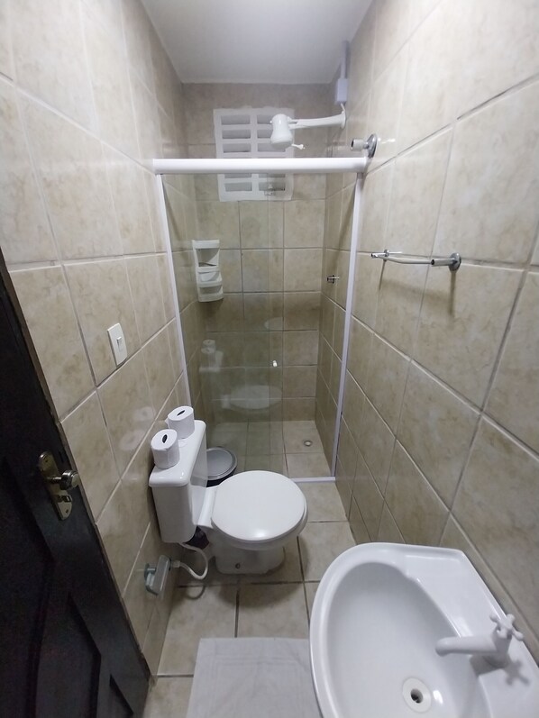 A small, tiled bathroom with a toilet, sink, and shower stall.