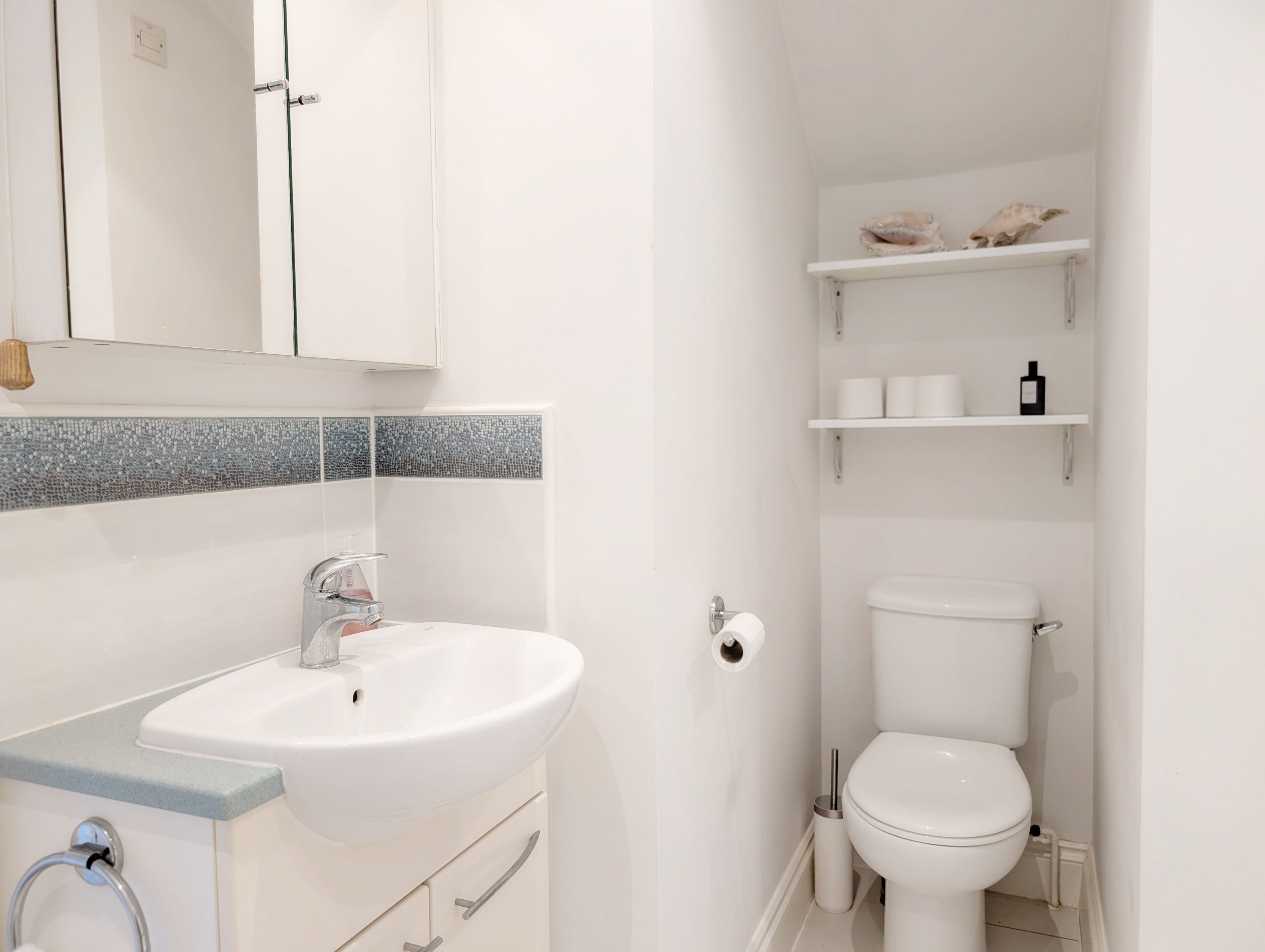 A modern bathroom with a white sink, a mirror, a toilet, and a shelf with toiletries.