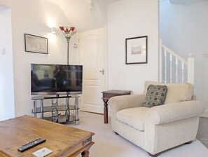 A living room with a television on a stand, a wooden coffee table, a beige sofa, and a staircase in the background. - 1a Tower Street - Emsworth -  a town house that sleeps 4 guests  in 2 bedrooms (Emsworth)
