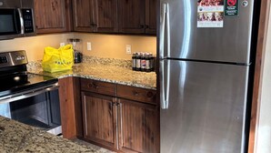A kitchen with wooden cabinets, a stainless steel refrigerator, a granite countertop, and a yellow bag.