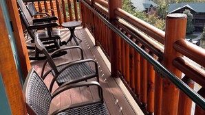 A wooden deck with metal chairs and a table, overlooking a forested area.
