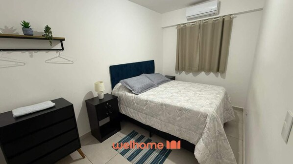 A bedroom with a bed, a nightstand, a dresser, a wall-mounted shelf with plants, and an air conditioning unit.