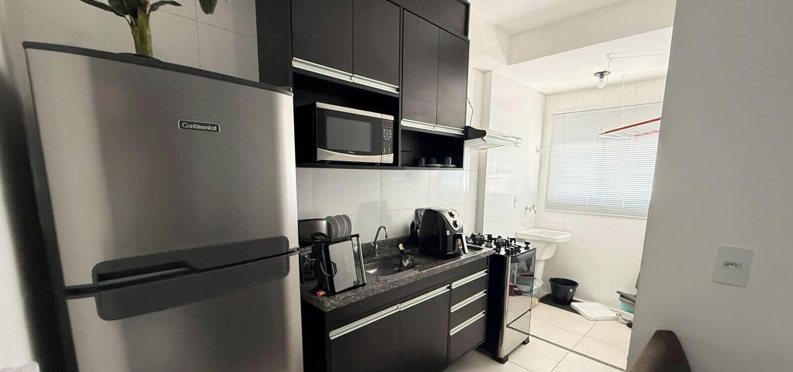 Una cocina compacta con un refrigerador de acero inoxidable, un microondas y una cafetera en la encimera.