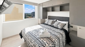 Une chambre moderne avec un lit, des rangements intégrés et une vue sur la ville.