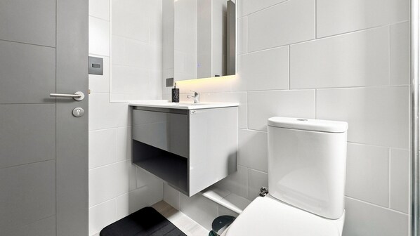 A modern bathroom with a toilet, a sink, and a mirror. - Oceana Suites Ñuñoa Central (Santiago)