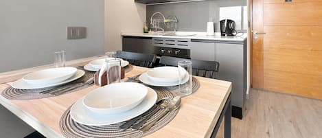 A modern kitchen with a dining table set for four, equipped with a microwave, oven, and coffee machine.