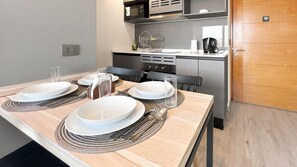 A modern kitchen with a dining table set for four, equipped with a microwave, oven, and coffee machine. - Oceana Suites Ñuñoa Central (Santiago)