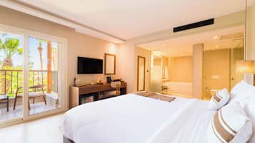 A hotel room with a bed, a desk with a TV, a bathroom, and a balcony with a chair.