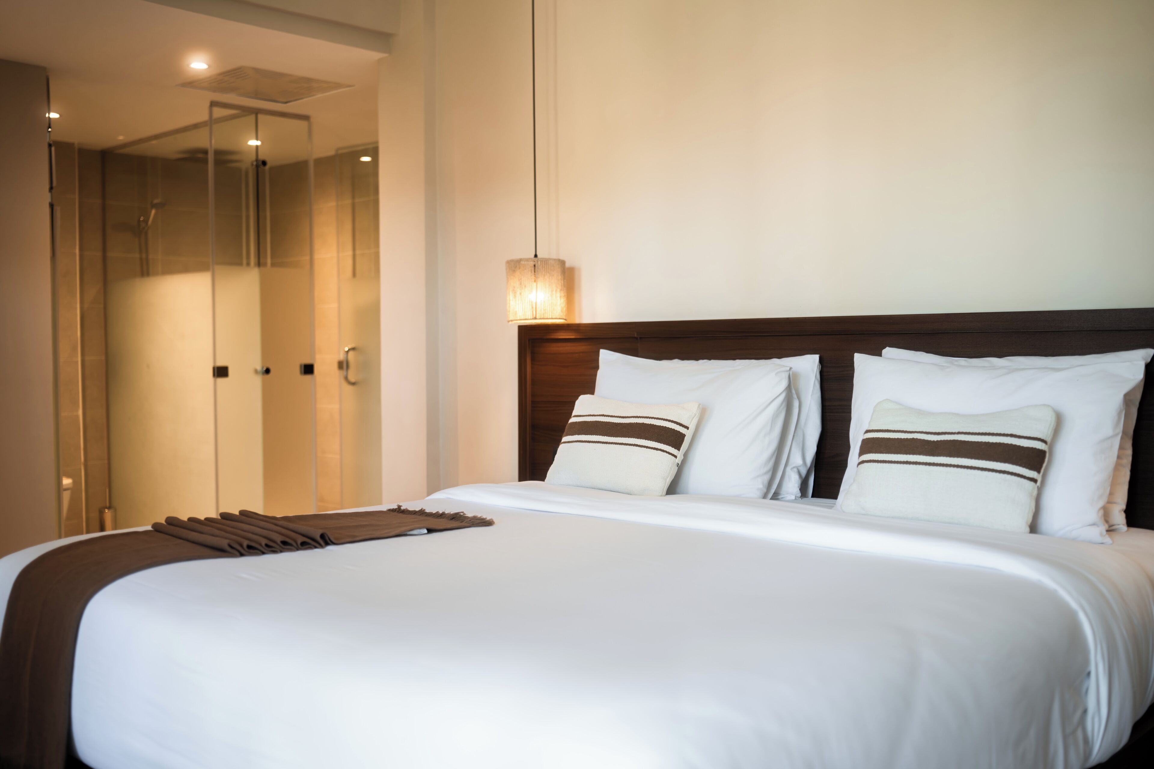 A hotel room with a large bed, a wooden headboard, and a glass shower enclosure.