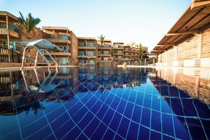 Una piscina di hotel con acqua cristallina, circondata da edifici a più piani con balconi e aree salotto all'aperto.