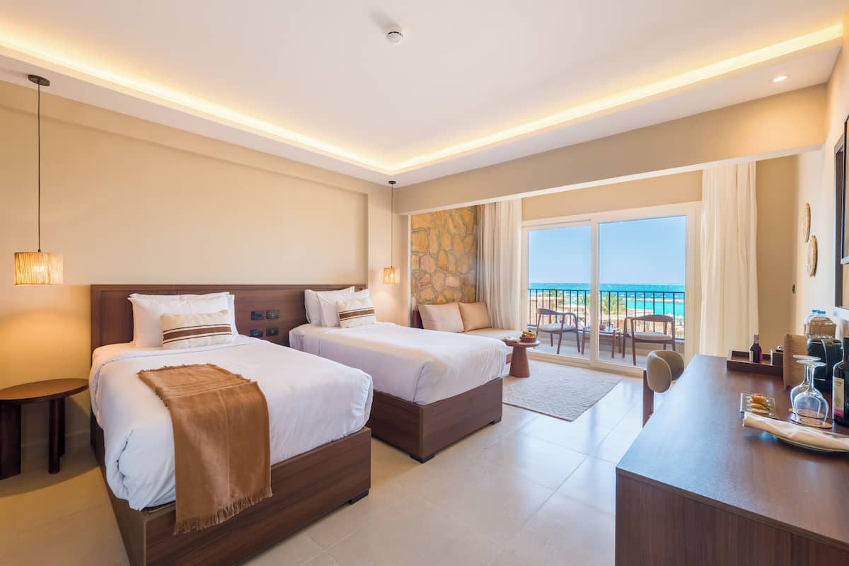 A hotel room with two beds, a desk, and a view of the ocean.