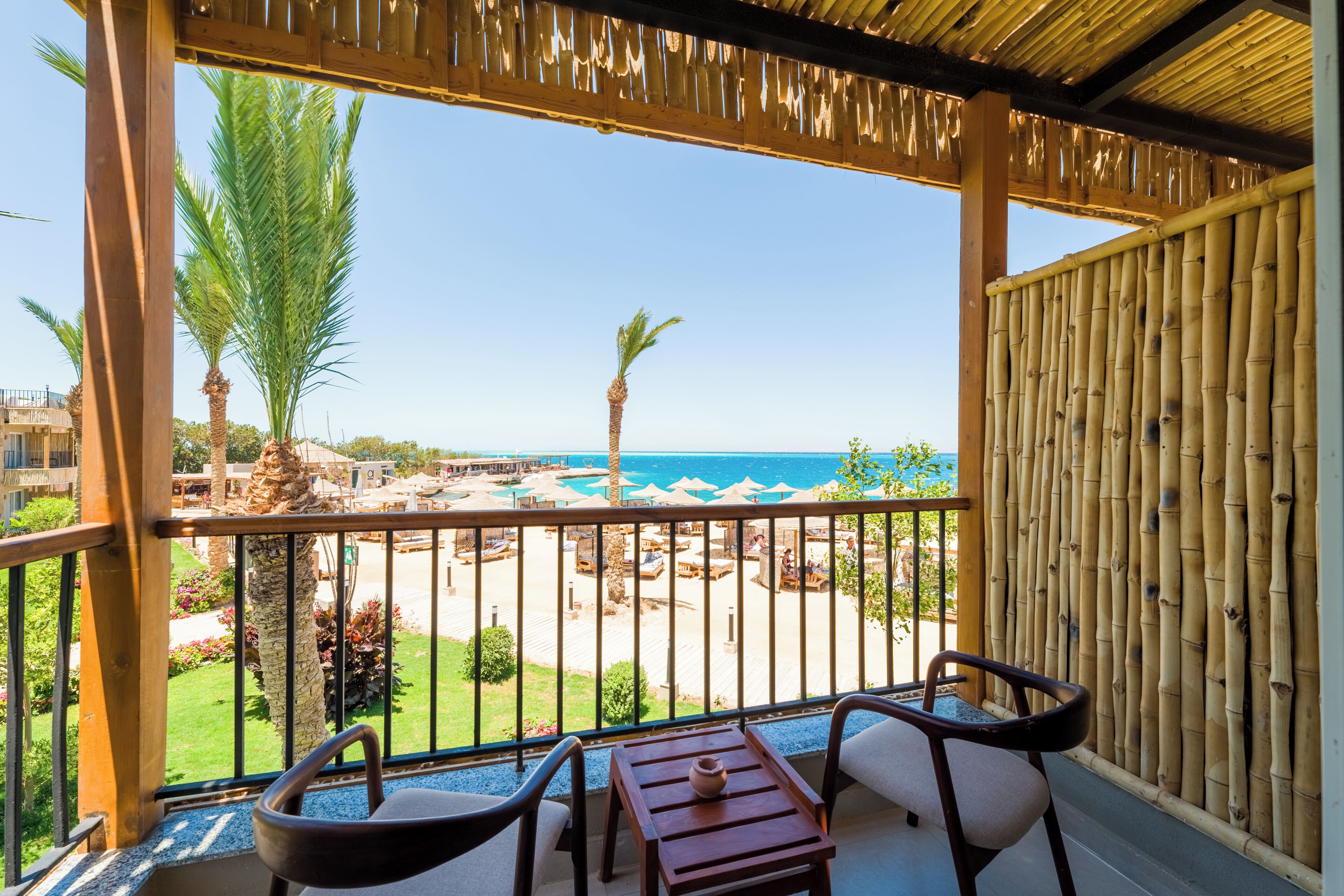 Un balcón con vista a la playa, mobiliario de madera y un muro de bambú.