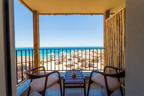 Un balcone con vista sulla spiaggia, sedie in legno, un tavolo e una recinzione in bambù.
