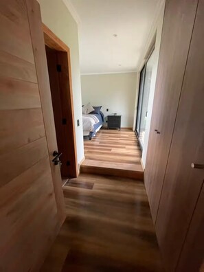 Un pasillo estrecho que conduce a un dormitorio con cama, mesita de noche y ventana.