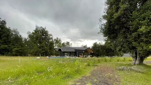 Une maison moderne avec une piscine, entourée d’un champ verdoyant et d’arbres.