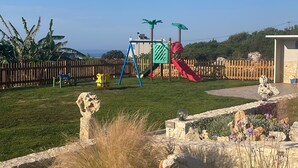 Une aire de jeux avec des toboggans et des structures d’escalade, entourée d’une clôture en bois et d’un mur en pierre.