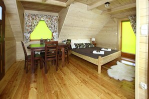 A cozy attic bedroom with a wooden floor, a bed with pillows, a desk with a chair, and a lamp.