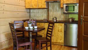 A wooden interior with a kitchen area featuring a microwave, a stainless steel refrigerator, and a wooden dining table with chairs.