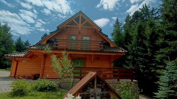 A wooden chalet with a sloped roof, a balcony, and a small garden area with flowers and a bird feeder.