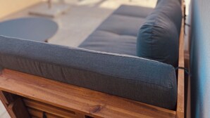 Een terras op het dak met een houten bank, een grijze gestoffeerde bank, een tafel met stoelen en een terras parasol.