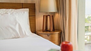 Een hotelkamer met een net opgemaakt bed, een bedlampje en een raam met gordijnen.
