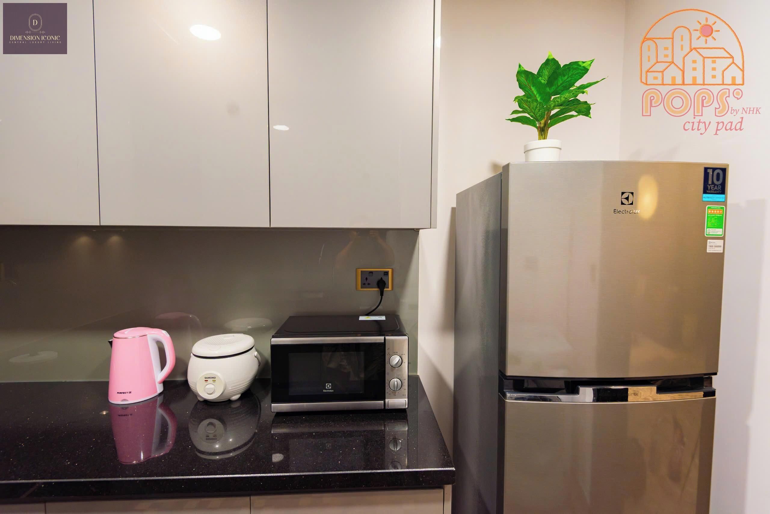 Una cocina con refrigerador, microondas y una tetera rosa en la encimera.