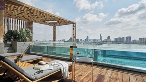 A rooftop infinity pool with a city skyline view, lounge chairs, and a wooden pergola.