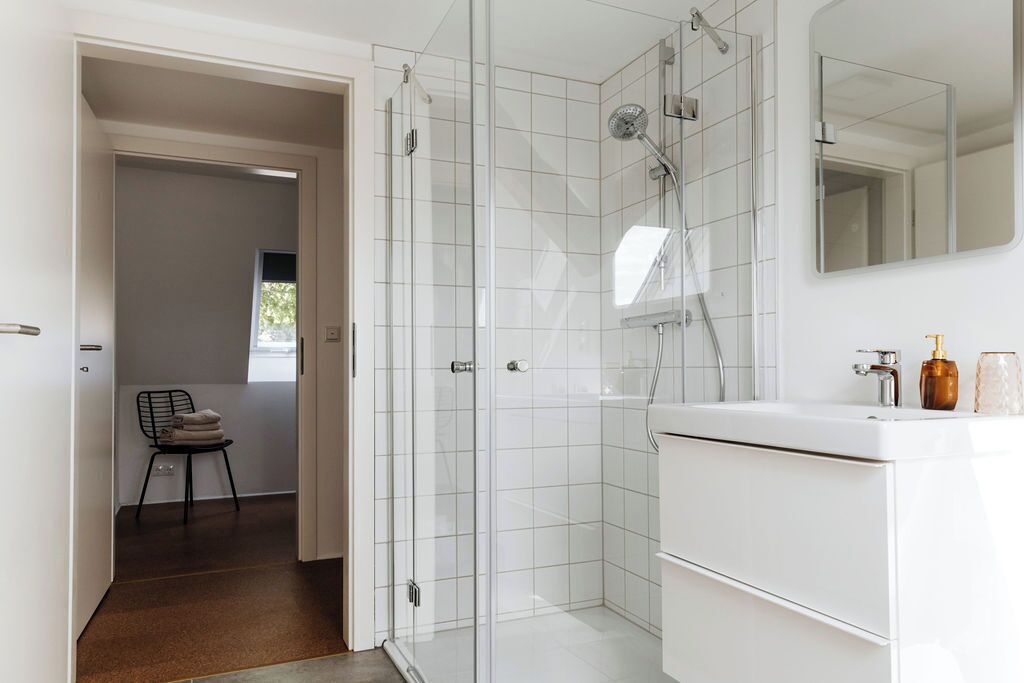 Een moderne badkamer met een douchecabine van glas, een witte wastafel en een spiegel erboven.
